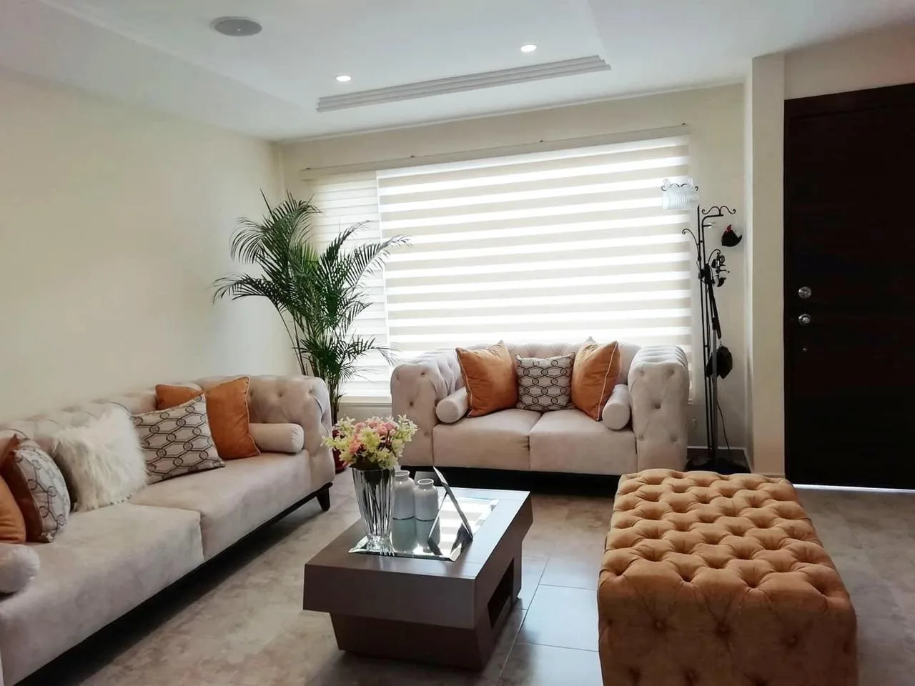 Sala a medida — sofá y loveseat capitoné crema con cojines naranja